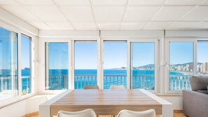 A spacious room with a large wooden table and white chairs, large windows with a view of the sea and cityscape. - Almadraba Penthouse (Benidorm)