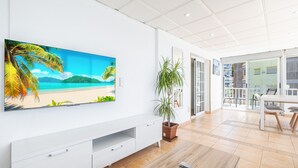 A modern living room with a large flat-screen TV, a wooden coffee table, a potted plant, and a sliding glass door leading to a balcony. - Almadraba Penthouse (Benidorm)