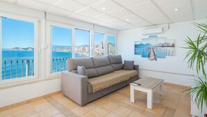 A living room with a sofa, a small table, and a view of the sea through large windows. - Almadraba Penthouse (Benidorm)
