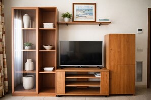 Un salon avec un téléviseur posé sur un meuble en bois, une bibliothèque, une plante en pot et un tableau encadré accroché au mur.