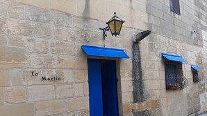 Un edificio de piedra con puerta azul y contraventanas, una farola y un cartel que dice 