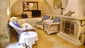 Una habitación acogedora con paredes de piedra, chimenea, dos sillones de mimbre, una mesita y un televisor.