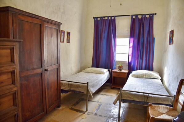 Een kamer met twee enkele bedden, een houten garderobe en een raam met paarse gordijnen.