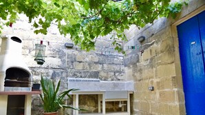 Un patio con un muro de piedra, una puerta azul, un lavamanos blanco y una planta en maceta.