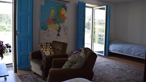 Ein Zimmer mit einem großen Fenster, einem Bett, einer Couch, einer Karte an der Wand und einer blauen Tür.