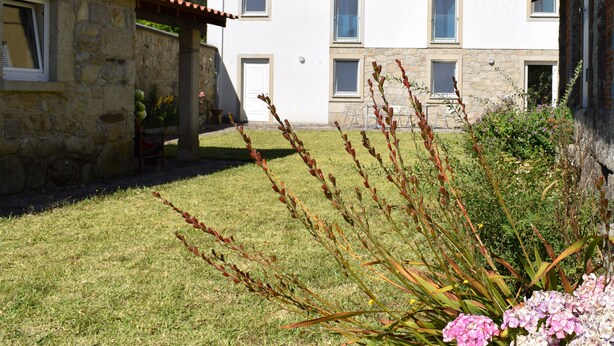 Ein Gebäude aus Stein mit rotem Ziegeldach, einem grünen Rasen und einem Blumenbeet mit rosa Blüten.