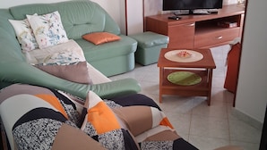 Een woonkamer met een groene bank, een houten tv-meubel en een wandklok.