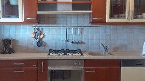 Een keuken met houten kastjes, een gasfornuis, een oven, een spoelbak en een tafel met een tafelkleed met bloemenmotief.