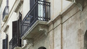 A building with a dark door, a small window with shutters, and a metal balcony railing.