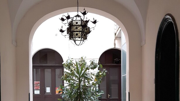 An arched corridor with a chandelier, potted plants, and a tiled floor.