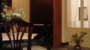A room with a wooden cabinet, a chair, a small table, and a window with curtains.