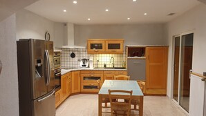 A compact kitchen with wooden cabinets, a stainless steel refrigerator, and a dining table with chairs.
