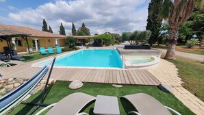 A swimming pool with a hot tub, lounge chairs, and a hammock.