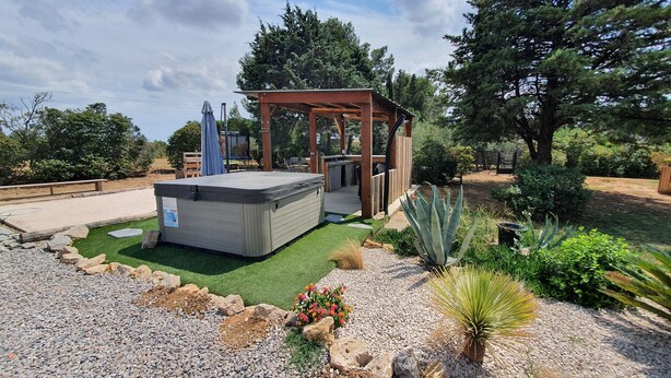 A hot tub with a wooden pergola, surrounded by a landscaped garden with rocks, gravel, and various plants.