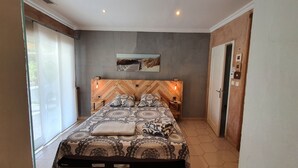 A bedroom with a large bed, a wooden headboard, a painting on the wall, and a door to the right.