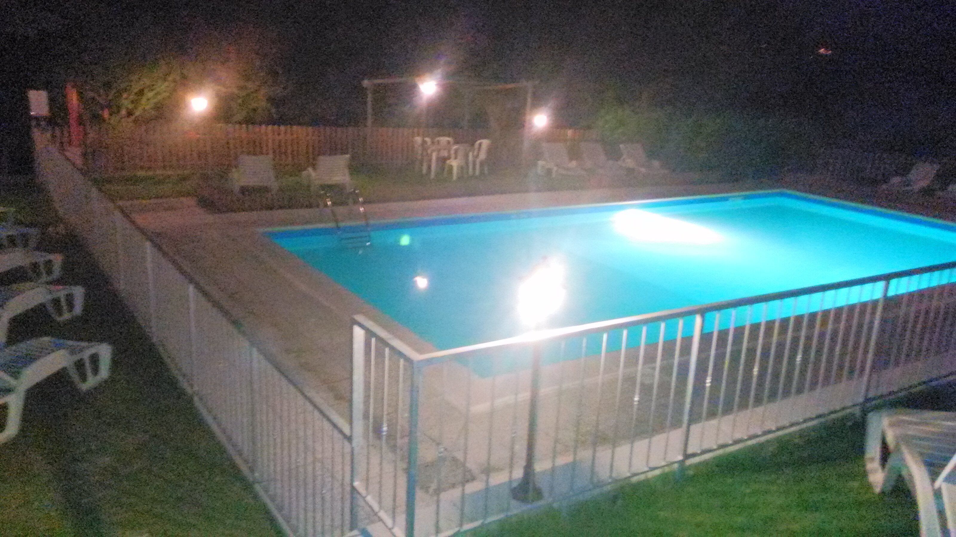 A rectangular swimming pool with a metal fence, surrounded by lawn chairs and a wooden deck.