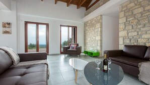 Un'ampia zona giorno con parete in pietra, un tavolo in vetro e calici da vino, e divani in pelle.