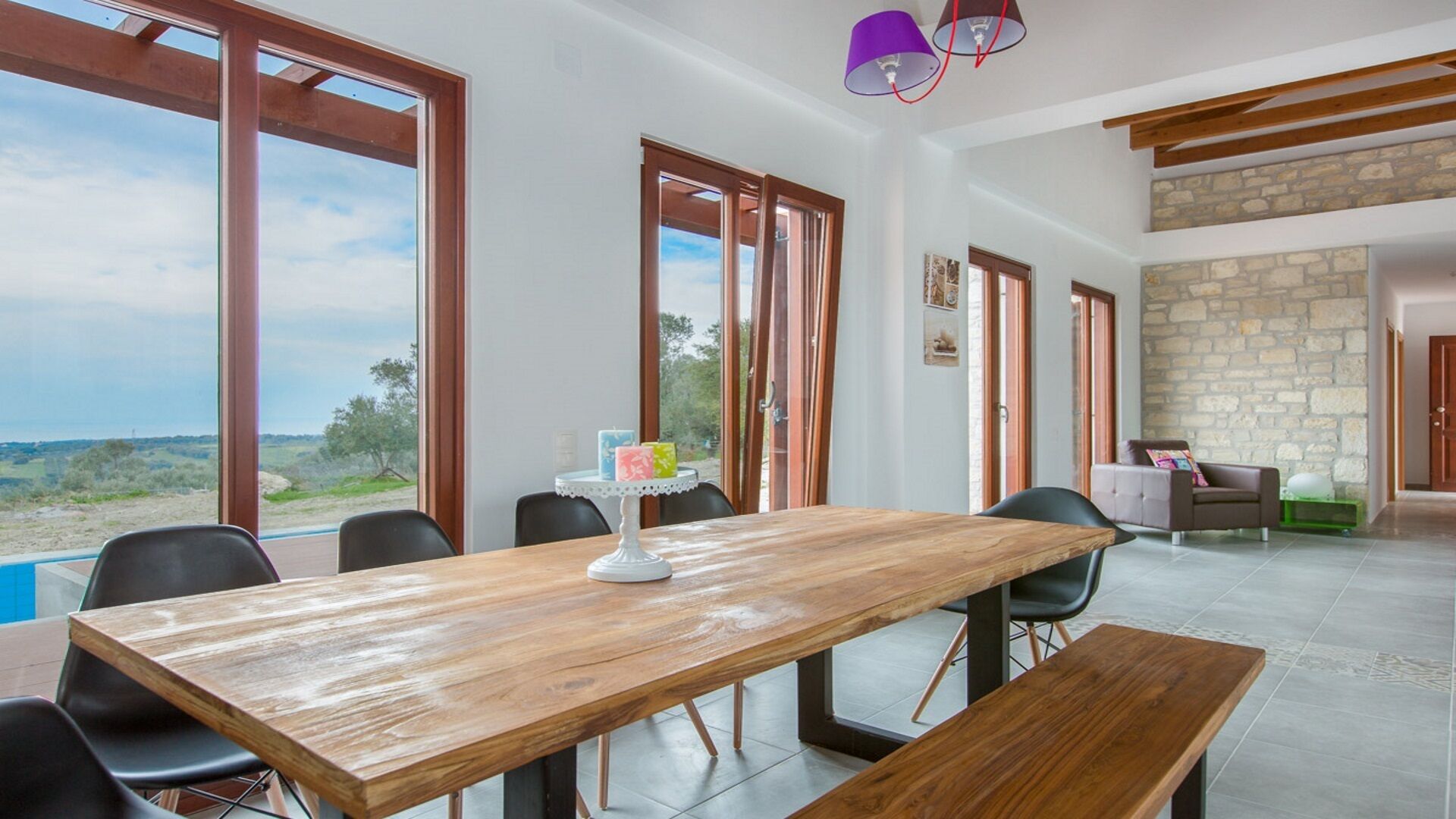 Un vaste espace dédié à la salle à manger, avec une table et des chaises en bois, de grandes fenêtres offrant une vue dégagée et un mur en pierre en arrière-plan.