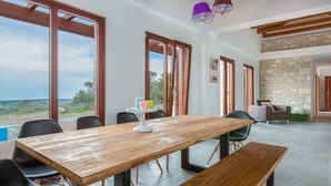 Un'ampia sala da pranzo con tavolo e sedie in legno, grandi finestre con vista e una parete in pietra sullo sfondo.
