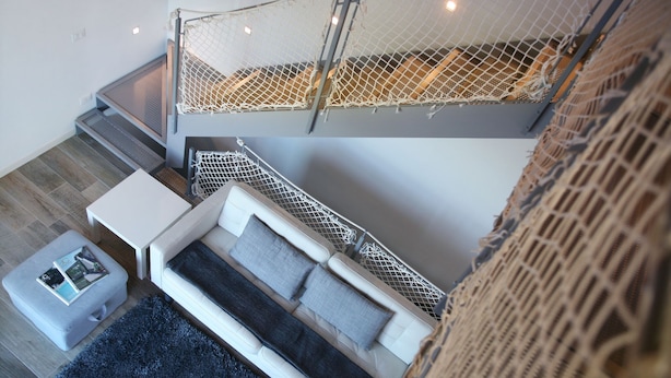 A modern living room with a white sofa, a small white table, and a grey ottoman. There is a grey rug on the floor. - Ville Golf - "The Golfette 2" (Manerba del Garda (BS))