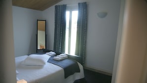 A hotel room with a bed, a bedside table with a lamp, a window with curtains, and a wall-mounted light fixture. - Ville Golf - "The Golfette 2" (Manerba del Garda (BS))