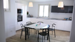A modern kitchen with white cabinets, a dining table with chairs, and a window with curtains. - Ville Golf - "The Golfette 2" (Manerba del Garda (BS))