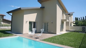 A modern house with a swimming pool, two lounge chairs, and a covered patio area. - Ville Golf - "The Golfette 2" (Manerba del Garda (BS))