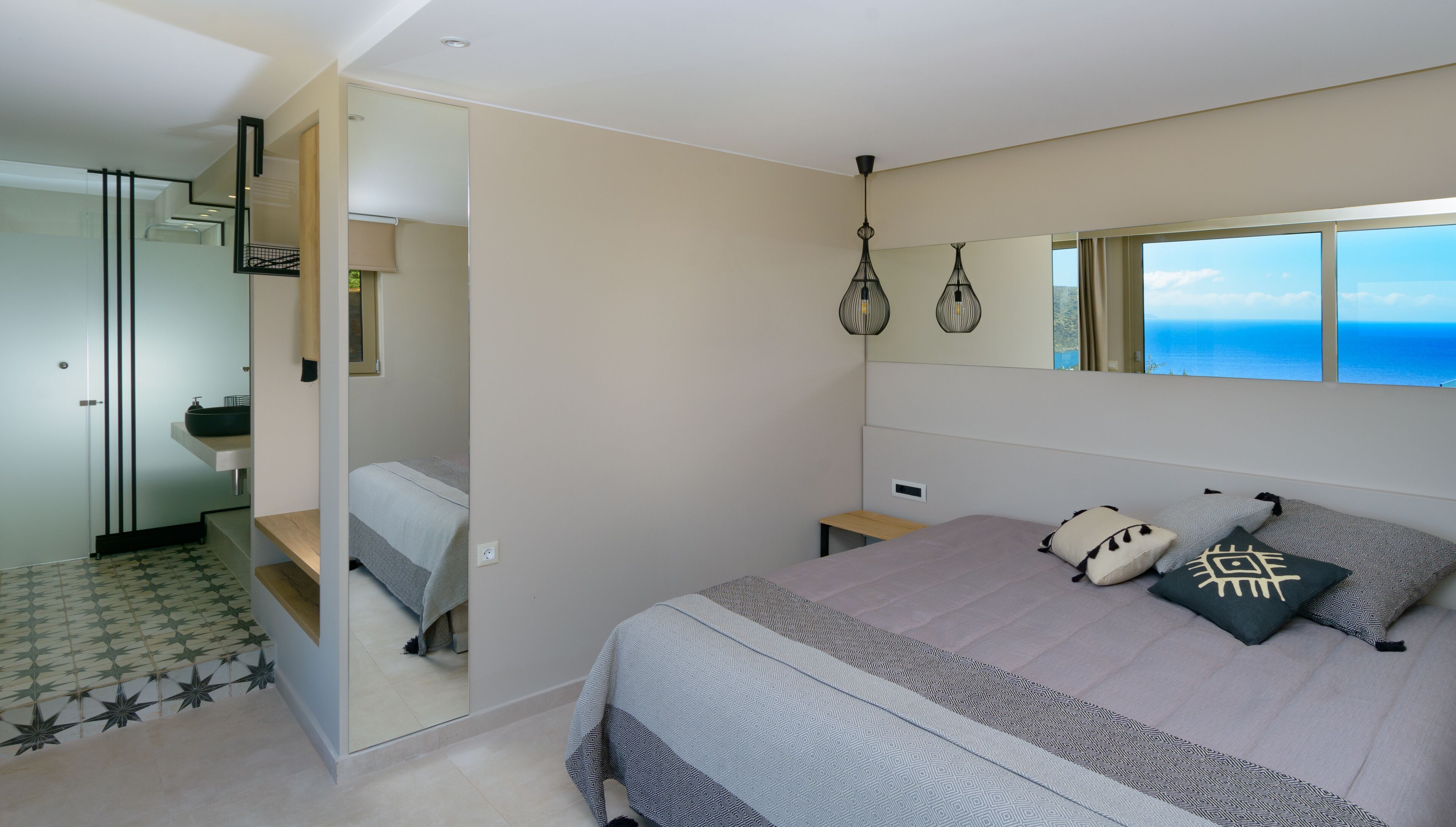 Een moderne slaapkamer met een groot bed, een badkamer met een spiegel en uitzicht op zee.