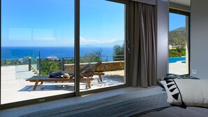 A bedroom with a large sliding glass door leading to a balcony with a view of the sea and mountains.