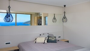 A bedroom with a large bed, a bedside table, a mirror, and a view of the sea.