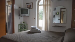 Un dormitorio con cama, televisor, espejo y ventana con cortinas.