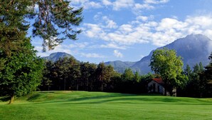 A golf course with a stone building, surrounded by trees and mountains in the background.