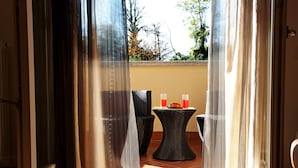 A room with a sliding glass door leading to an outdoor seating area with two wicker tables and chairs, and a small table with two glasses of orange juice and a croissant.