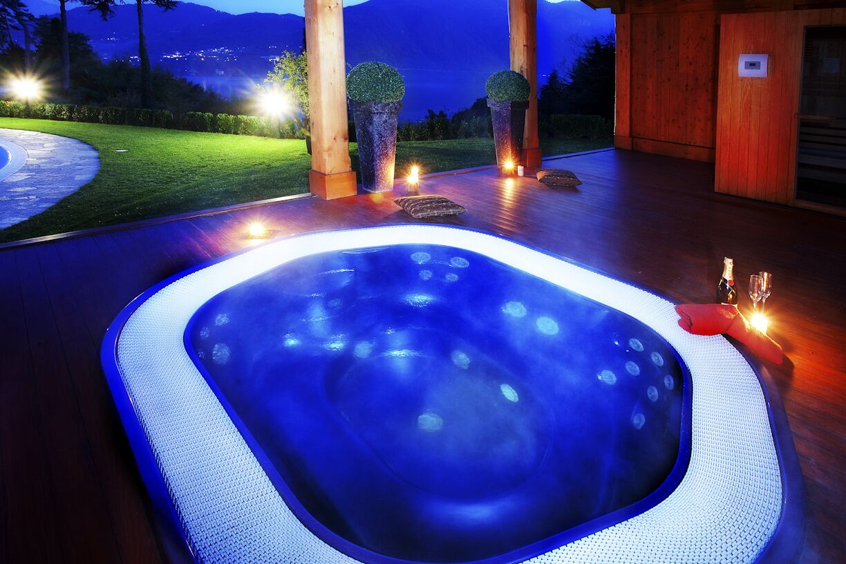 Un jacuzzi con vistas a un jardín ajardinado y montañas al fondo.