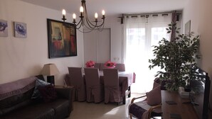 A living room with a sofa, a dining table with chairs, a chandelier, a painting, and a potted plant. - Lovely Apartment in Nice - Book now for great Prices! (Nice)