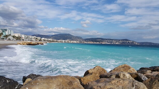 A coastal view with clear turquoise waters, rocky shoreline, and a cityscape in the background. - Lovely Apartment in Nice - Book now for great Prices! (Nice)