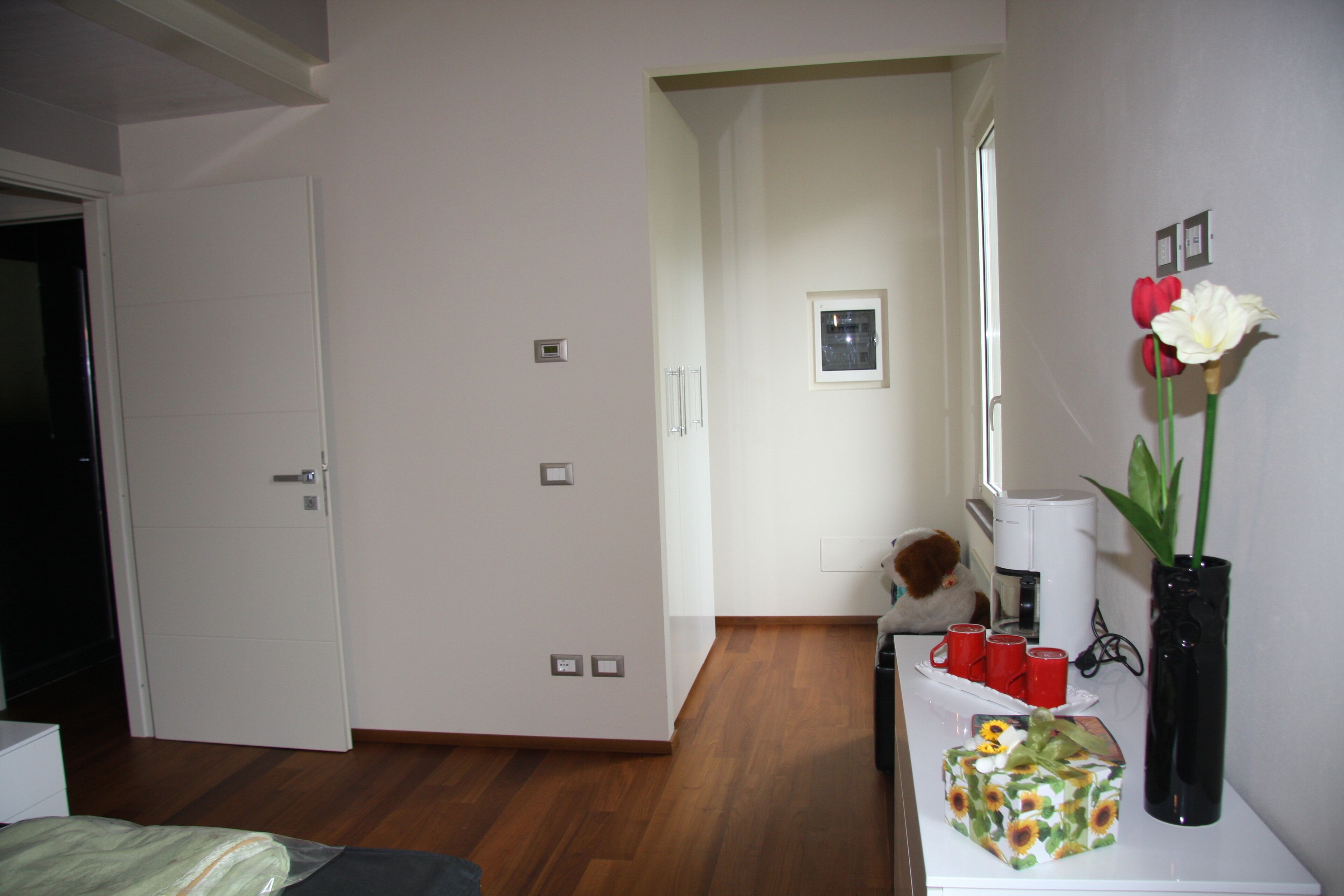 Une chambre d’hôtel avec un plancher en bois, un lit, un bureau agrémenté d’un vase de fleurs et une machine à café.