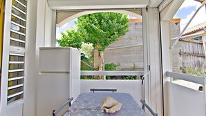Een balkon met een tafel, stoelen, een koelkast en een grote boom op de achtergrond.