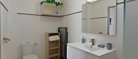 A compact bathroom with a toilet, a sink, a mirror, a shelf with toiletries, and a small plant.