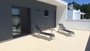 A modern outdoor patio with two sun loungers and a small table, a sliding glass door leading to an interior space, and a white building with a satellite dish. - Modern villa with swimming pool and terrace, near the Bay of Obidos (Nadadouro)