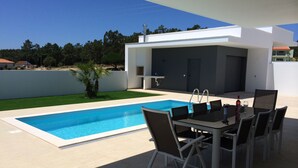 A modern outdoor pool area with a rectangular pool, a dining table with chairs, and a small patio table with wine glasses and a bottle. - Modern villa with swimming pool and terrace, near the Bay of Obidos (Nadadouro)