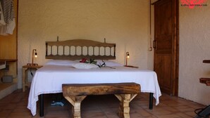Ein Bett mit Holz-Kopfstück, ein Nachttisch mit Lampe und eine Bank.
