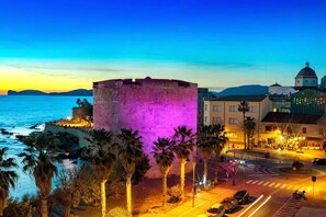 Un edificio histórico con una torre redonda, palmeras y vista al mar.