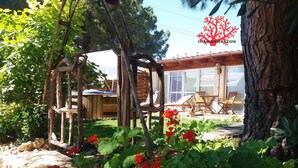 Eine hölzerne Pergola, ein überdachter Sitzbereich mit Stühlen und ein großer Baumstamm.