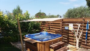 Ein Whirlpool in einem Garten mit Holzboden, umgeben von Grünpflanzen und einem Holzzaun.