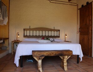 Una cama con cabecera de madera, una mesita de noche con lámpara y un banco.