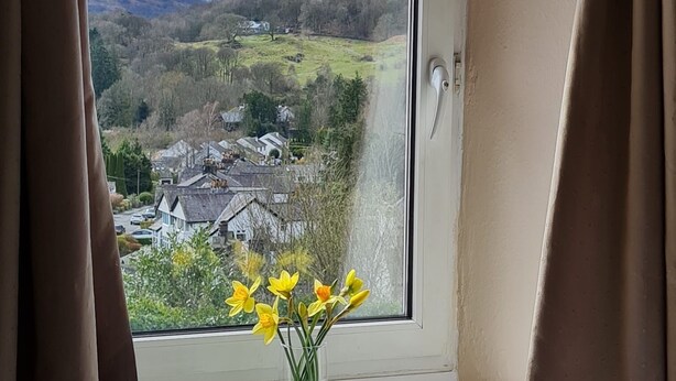 A window with a view of a valley, a vase with yellow flowers, and brown curtains. - Bluehill Cottage,Ambleside, Stunning Views, parking, 0.8ml to Ambleside centre (Ambleside)