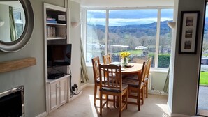 A dining area with a table and chairs, a bookshelf, a fireplace, and a view of the outdoors. - Bluehill Cottage,Ambleside, Stunning Views, parking, 0.8ml to Ambleside centre (Ambleside)