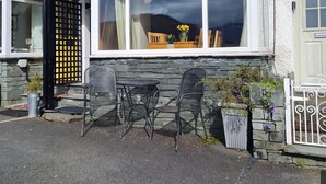 A building with a large window, a door, and a small outdoor seating area with chairs and a table. - Bluehill Cottage,Ambleside, Stunning Views, parking, 0.8ml to Ambleside centre (Ambleside)