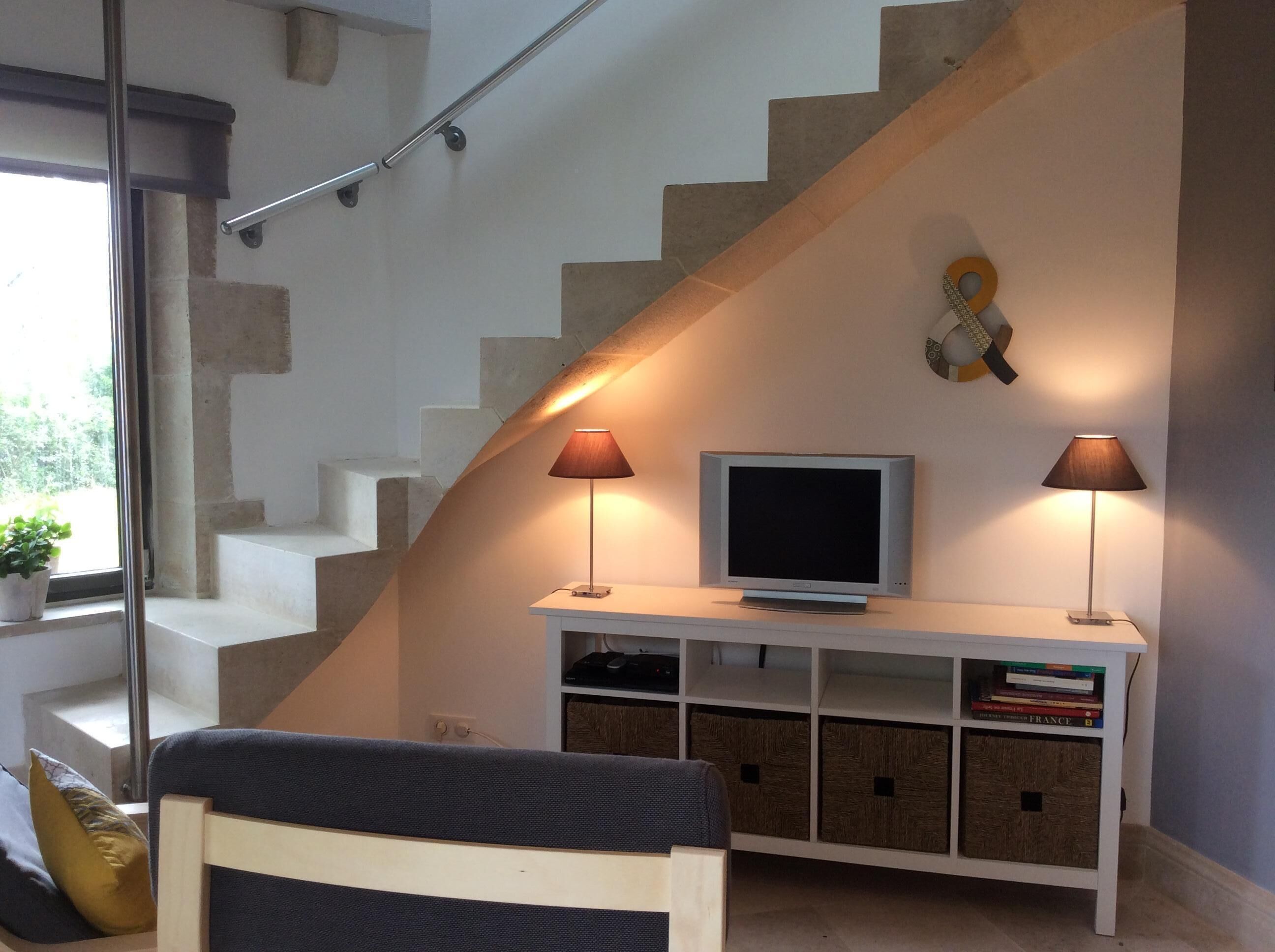 Een moderne woonkamer met een trap, een flatscreen televisie, twee lampen en een boekenplank.